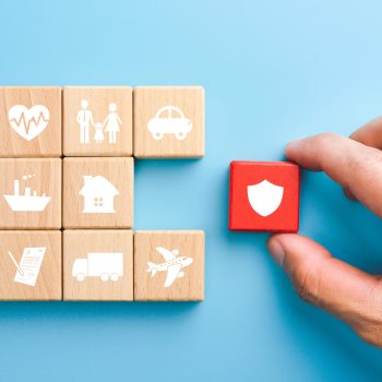 Hand holding red wooden blocks with insurance icons. family, life, car, travel, health and house insurance icons, blue background, Insurance concept